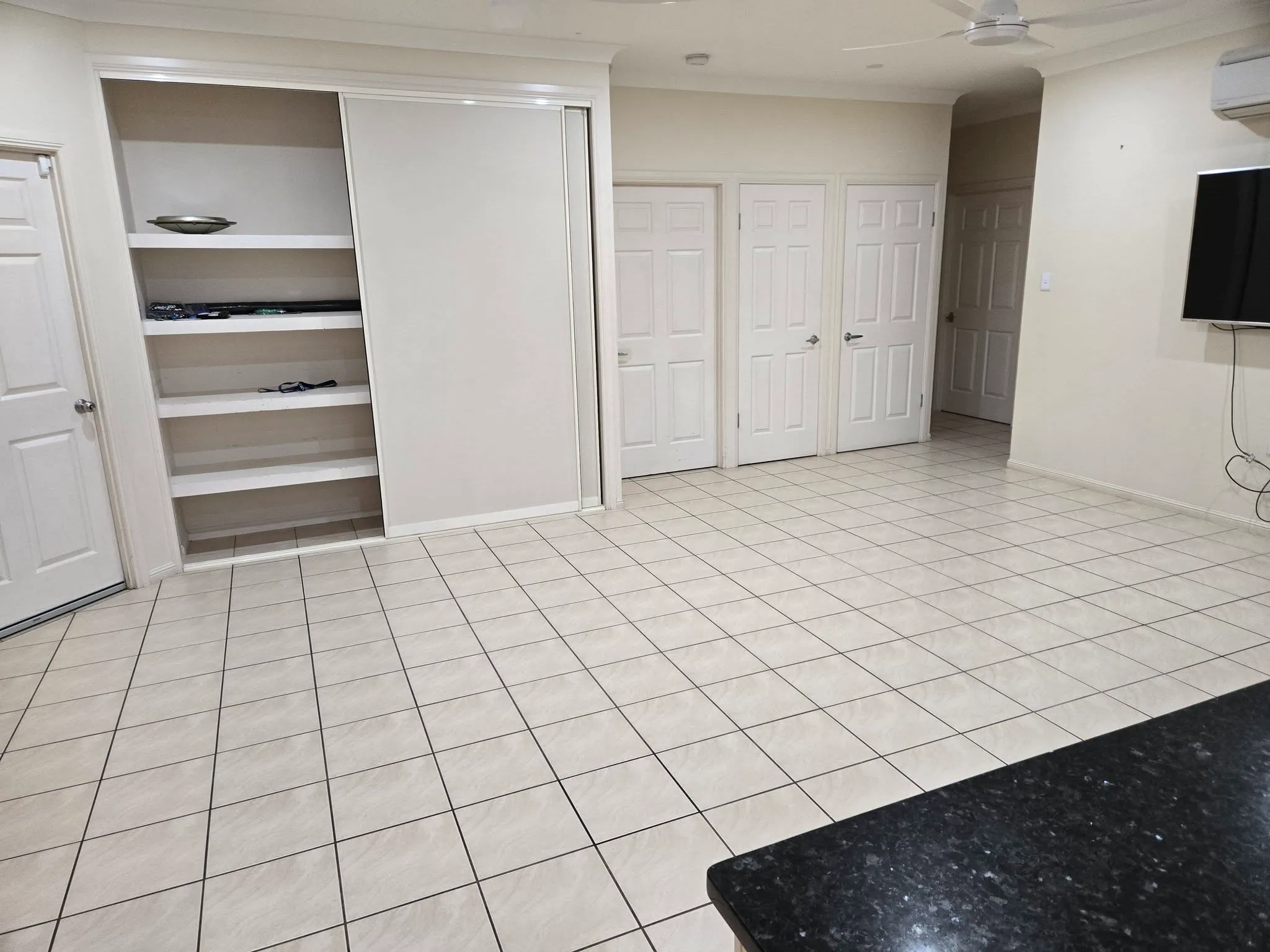 Vacant tiled living area with built-in shelving and wall-mounted TV